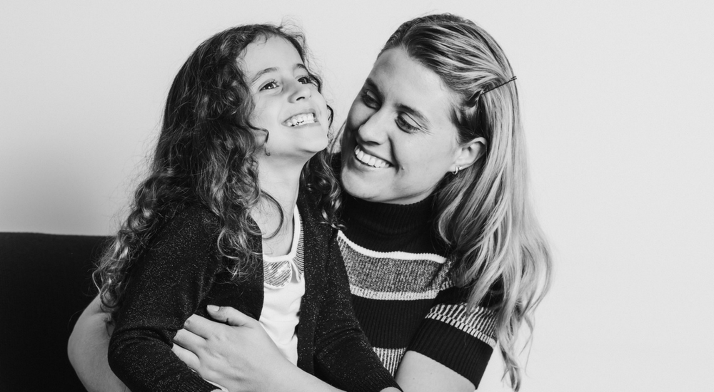 A daughter sitting on her mother's lap, they are laughing and smiling together